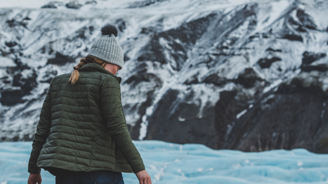 Female observing glacier in puffy green jacket and knit cap