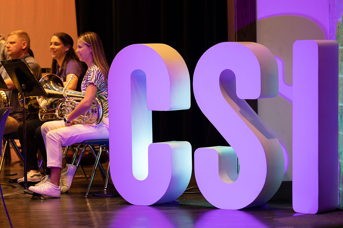 Large CSI letters statue on stage with student performers.